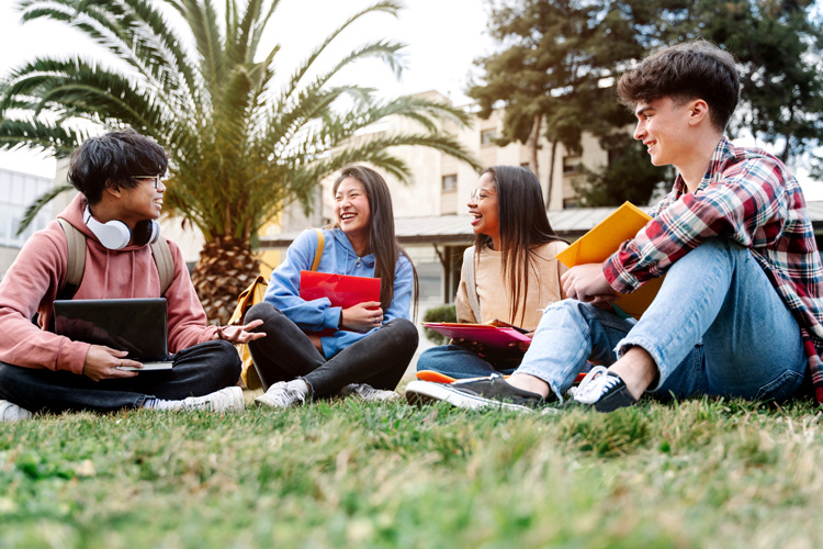 Group of multiracial international exchange university students sitting on the grass in the campus.