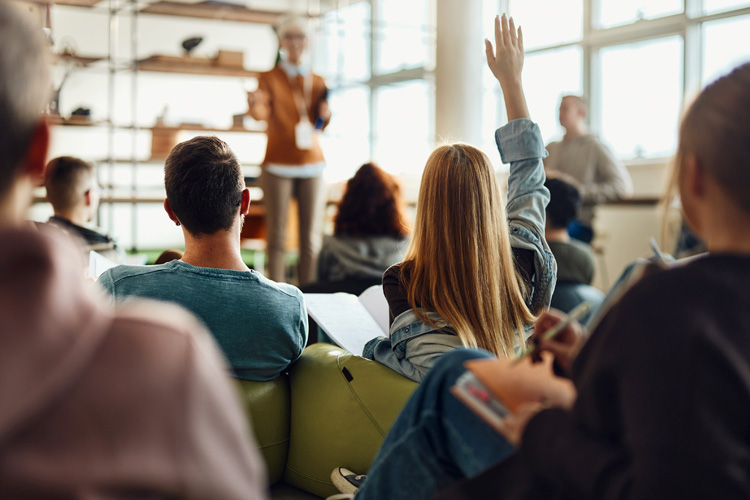 A student raising her hand in class for teacher calls on insightful contribution.