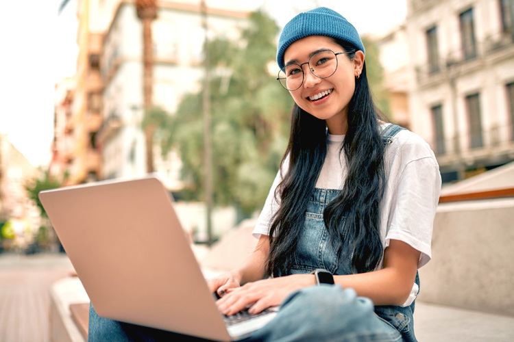 Asian female overseas student on city streets with her laptop.