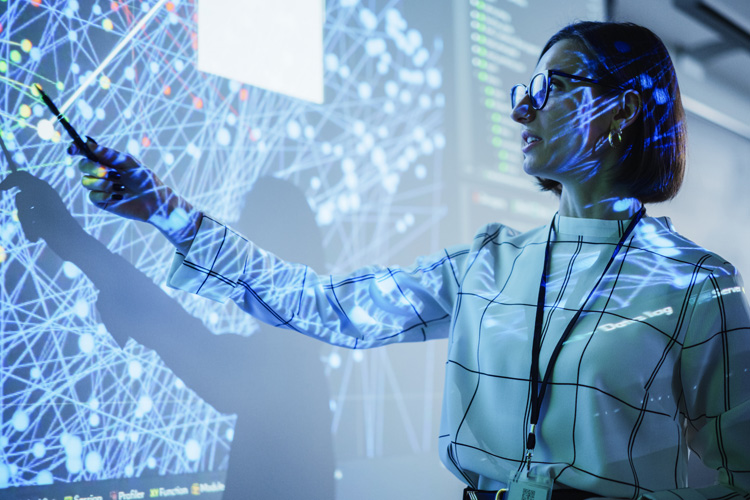 A young female teacher presents data science in a dim auditorium with slides.